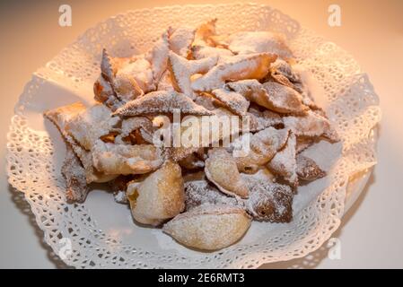 Ali d'angelo o bugie o frappe o chiacchiere su carta tovagliata rotonda decorata tovagliolo.tradizione alimentare carnevale italiano. Luce calda Foto Stock