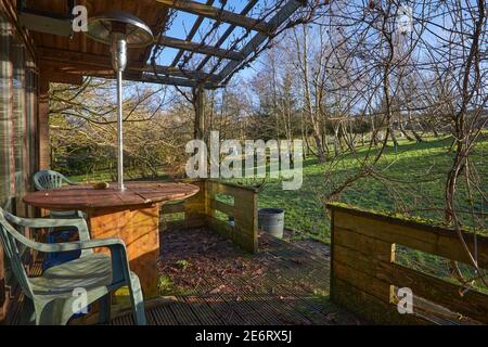 Tavolo in legno, sedie in plastica e riscaldamento a gas forniscono un'area salotto esterna nella casa estiva sulla piccola brughiera Foto Stock