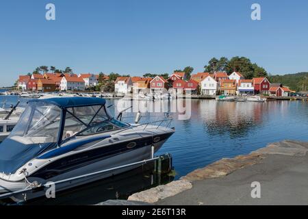 Piccolo yacht blu e bianco e case colorate al Porto del bellissimo villaggio di pescatori Svenevig nel sud della Norvegia Foto Stock