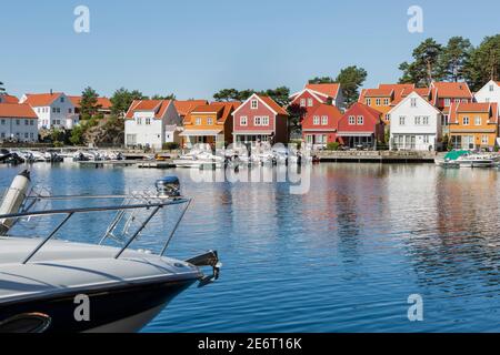 Piccolo yacht blu e bianco e case colorate al Porto del bellissimo villaggio di pescatori Svenevig nel sud della Norvegia Foto Stock