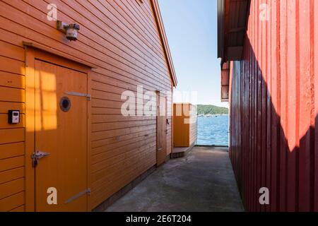 vista tra una casetta di legno arancione e una casetta di legno rosso il mare nel porto del bellissimo villaggio di pescatori Svenevig nella Norvegia meridionale Foto Stock