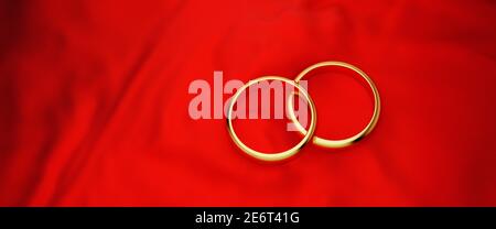 Due anelli di nozze dorati su uno sfondo in tessuto rosso. Dimensione banner Web. Foto Stock