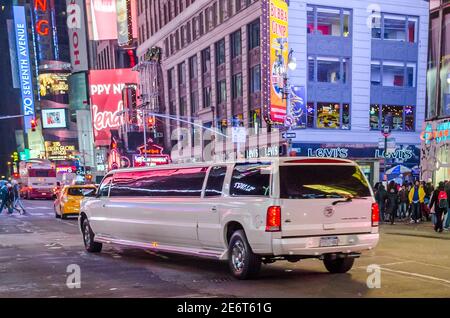 Limousine bianca che passa attraverso Times Square a Manhattan, New York City, USA. Via affollata con schermi animati e affissioni brillanti Foto Stock