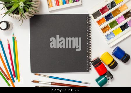 Libro di schizzo nero su una tabella bianca con materiali di disegno. Foto Stock