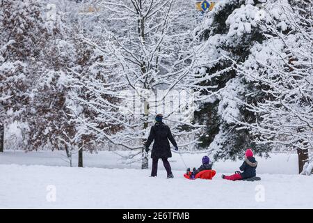 Vilnius, Lituania, 28 gennaio 2021. Madre con due bambini su slitte passeggiate nel parco innevato Foto Stock