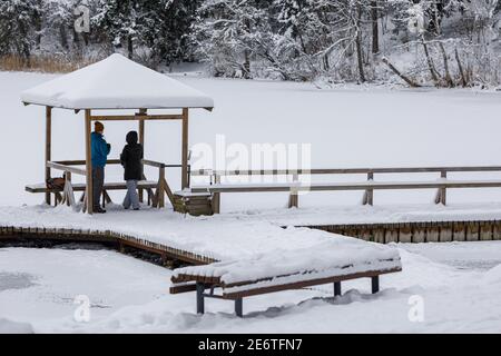 Vilnius, Lituania, 28 gennaio 2021. Due persone nel gazebo innevato su un lago ghiacciato con un ponte di legno nel parco pubblico Foto Stock