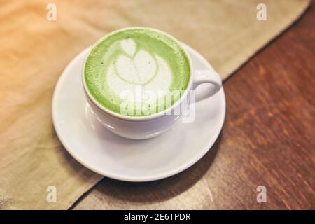 Tazza di latte matcha su sfondo di legno e un tovagliolo beige in un caffè con spazio per le copie. Foto di alta qualità Foto Stock