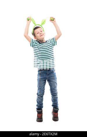 Felice eccitato giovane ragazzo con Pasqua coniglietto orecchie danzare e saltare con mani sollevate. Lunghezza intera isolata su sfondo bianco. Foto Stock