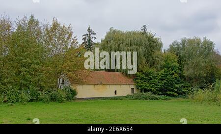 Prato verde con vecchio fienile di pietra e alberi nel Campagna fiamminga Foto Stock