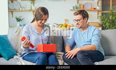 Ordinazione di regali online. Un uomo dà a una donna un regalo che ha ordinato attraverso il luogo, un deposito in linea. La ragazza prende fuori un regalo rosso da un cartone Foto Stock