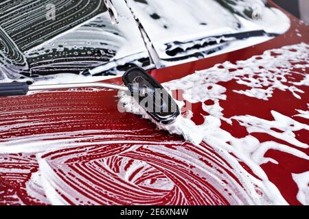 Auto rossa lavata in autolavaggio, dettaglio da spazzolare lasciando colpi sul cappuccio in schiuma bianca Foto Stock