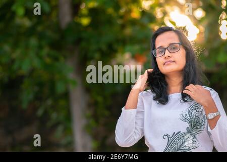 Lunga ragazza dai capelli neri bella che spinge i capelli indietro, in posa per una macchina fotografica mentre il sole è dietro la schiena e che brilla attraverso il gre Foto Stock