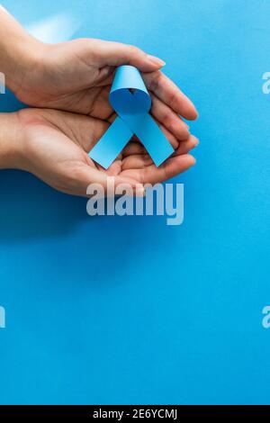 Colpo verticale delle mani femminili che tengono il nastro blu di consapevolezza sopra sfondo blu Foto Stock