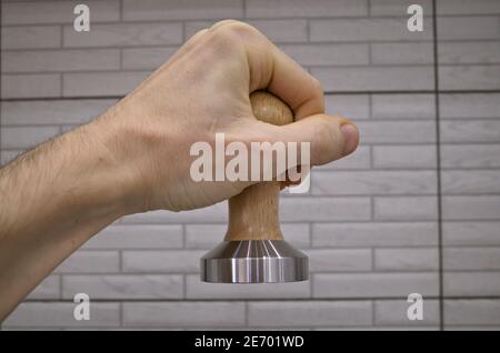 Manomissione a mano maschile per la pressione del caffè macinato per la preparazione di una bevanda espresso in una macchina da caffè. Apparecchiatura barista antimanomissione con manico in legno Foto Stock
