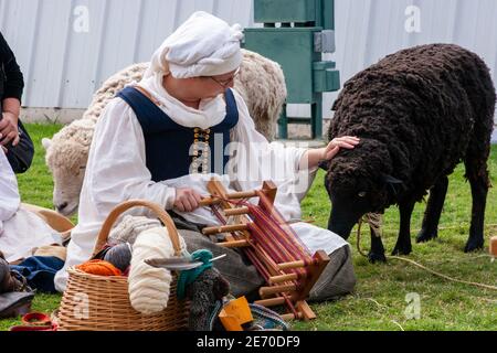 Donna in costume medievale che accarezzano una pecora mentre fa indumenti di lana Foto Stock