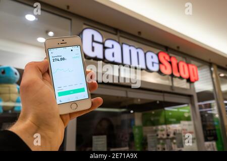 Gamestop GME stock nell'app di trading online di broker Trade Republic su uno schermo del telefono cellulare. Di fronte a un negozio GameStop. Foto Stock