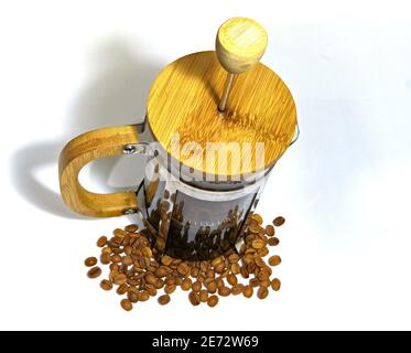 Macchina per il caffè French press sulla terra bianca. Caffè arabo fagioli fondo della pressa francese e caffè cotto all'interno del lato di vetro della pressa. Foto Stock