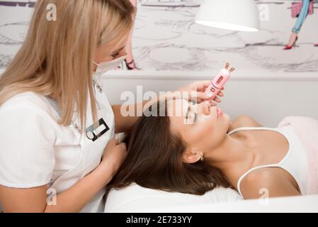 Concetto di bellezza. Processo di estensione del ciglia. Bella ragazza dai capelli scuri si trova su un divano nell'ufficio del maestro eyelash. Foto Stock