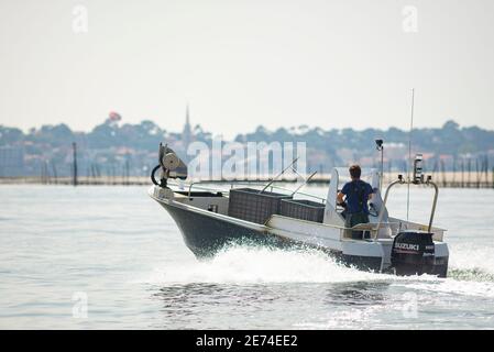 Il pescatore su un motoscafo sta andando l'allevamento di ostriche nel Bassin d'Arcachon, Gironde, Francia. Caselle vuote sull'imbarcazione. Foto Stock