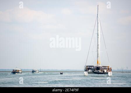 Il grande multiscafo sta navigando nel Bassin d'Arcachon. Tre motorboars stanno passando vicino al catamarano Foto Stock