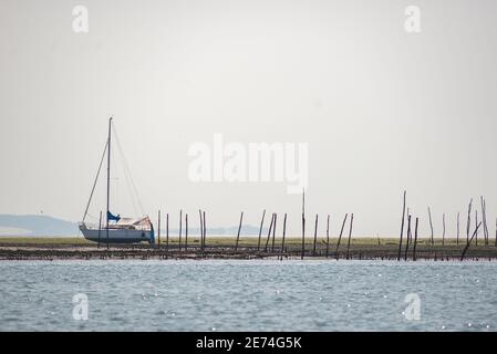 Una barca a vela in spiaggia su una riva di sabbia nella baia di Arcachon, Gironde, Francia, Europa. Pali di legno e trappole di ostriche sulla costa Foto Stock