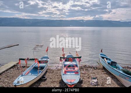 Piccole e blu barche vicino alla costa del lago di Uluabat in Turchia. Piccola bandiera turca sulla barca con lago e sfondo di montagna. Bursa. Golyazi. Foto Stock