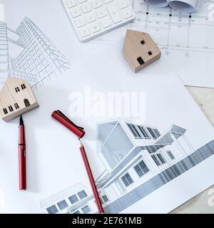 Rotoli di carta, disegni di costruzione, calcolatrici e modelli di case in legno su pavimenti in cemento. Foto Stock