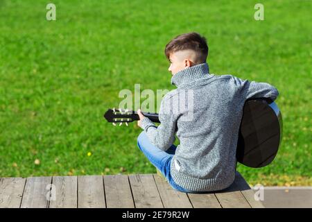 teen boy suona la chitarra acustica nera in un giorno d'autunno Nel Parco Foto Stock