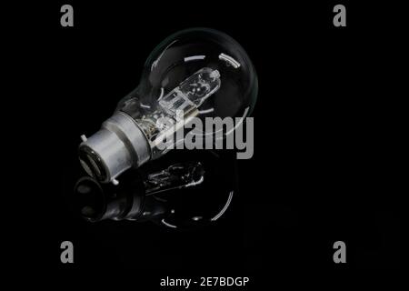Primo piano di una lampadina alogena in vetro trasparente appoggiata una superficie riflettente nera Foto Stock