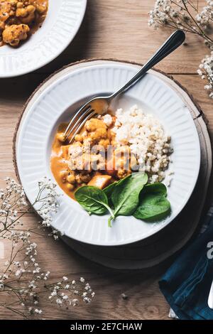 Ceci e cavolfiori al curry con riso marrone e spinaci su sfondo ligneo. Foto Stock