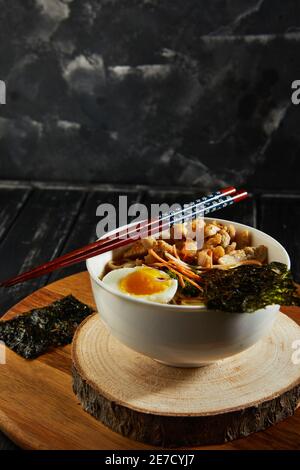 Zuppa giapponese di ramen con pollo, uovo, aglio e tagliatelle su sfondo di legno scuro. Tagliatelle asiatiche di misto Ramen. Foto Stock