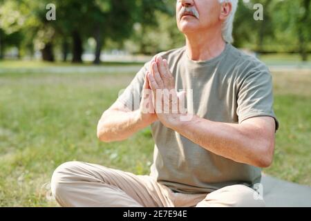 Uomo anziano seduto in posizione lotus e rilassante durante lo yoga all'aperto Foto Stock