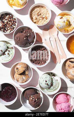 Colpo verticale di diversi gusti di gelato in luce dura su una tavola di legno verniciata bianca Foto Stock