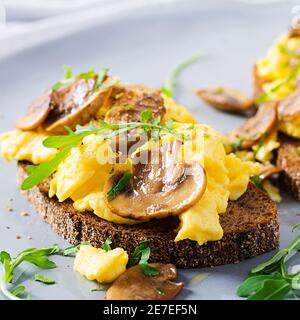 Uova strapazzate e funghi fritti sul pane. Colazione fatta in casa o pasto brunch - uova strapazzate e panini con funghi. Foto Stock