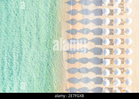 Vista da sopra, splendida vista aerea di un vuoto incredibile spiaggia bianca con ombrelloni bianchi e turchesi acque chiare durante il tramonto. Foto Stock