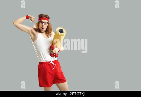 Uomo divertente con stuoia e manubri che mostra i suoi muscoli sorpresi a quanto grandi sono cresciuti Foto Stock