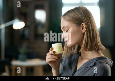 Giovane bella femmina con capelli biondi godendo di odore naturale prodotto cosmetico fatto a mano in vasetto di plastica piccolo prima di applicarlo sulla pelle Foto Stock