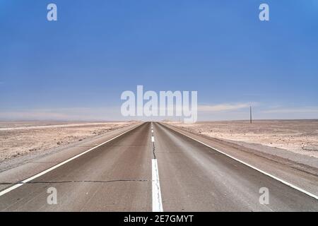 Strada scura e nera in asfalto che non conduce direttamente all'orizzonte nel deserto di atacama del Cile in Sud America Foto Stock