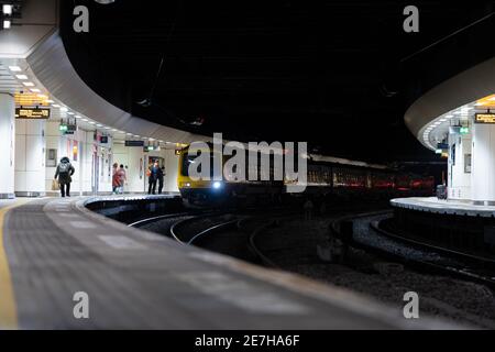 Treno passeggeri con luci in attesa a due piattaforme sotterranee di notte durante la chiusura pandemica con pendolari e acquirenti imbarco carrello Foto Stock