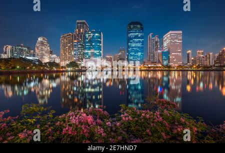 Lago con fiori viola nel parco cittadino sotto i grattacieli di notte. Benjakiti Park a Bangkok, Thailandia Foto Stock