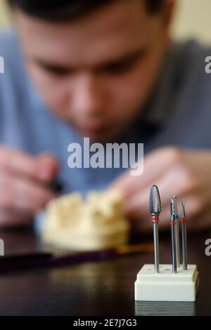 Tecnico dentale modellando le corone dei denti con cera calda. Luogo di lavoro di un tecnico odontoiatrico. Concentrarsi sugli strumenti dentali Foto Stock