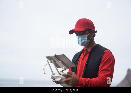 Scatola di volo del corriere dell'uomo per la consegna con il drone mentre indossa Maschera di sicurezza - Messa a fuoco sul viso Foto Stock