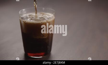 versare la cola su cubetti di ghiaccio nel bicchiere sul tavolo in noce con spazio per la copia, foto ampia Foto Stock