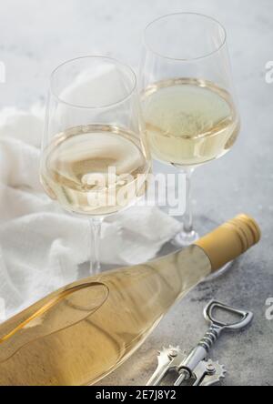 Bottiglia di vino bianco con due bicchieri di cristallo e cavatappi in acciaio su sfondo chiaro. Foto Stock
