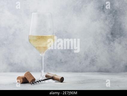 Bicchiere di vino bianco estivo con tappi e cavatappi su sfondo chiaro. Foto Stock