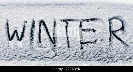 parola inverno scritto con il dito in neve fresca su auto finestra Foto Stock