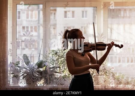 Silhouette di una giovane ragazza, un musicista. Suonare il violino sullo sfondo della finestra. Foto Stock