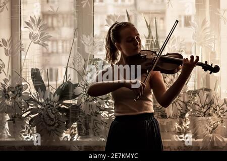 Silhouette di una giovane ragazza, un musicista. Suonare il violino sullo sfondo della finestra. Foto Stock