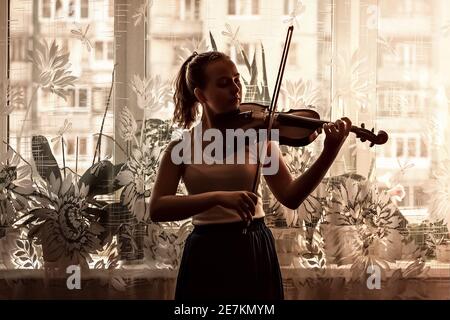 Silhouette di una giovane ragazza, un musicista. Suonare il violino sullo sfondo della finestra. Foto Stock