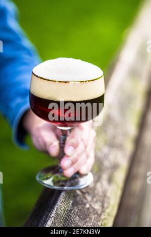 Versare la birra ghiacciata in un bicchiere durante il tramonto in campagna su una recinzione di legno Foto Stock